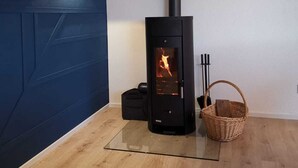 A modern room with a wood-burning stove, a blue accent wall, and a glass table. - Unique and modern apartment with designer bathroom and terrace (Petting)