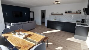 A modern kitchen with a dining area, featuring a wooden dining table, grey chairs, and a grey sofa. - Unique and modern apartment with designer bathroom and terrace (Petting)
