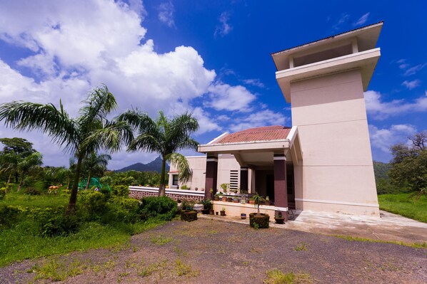 A modern building with a large porch, surrounded by lush greenery and palm trees. - Shetty Farms (Dahanu)