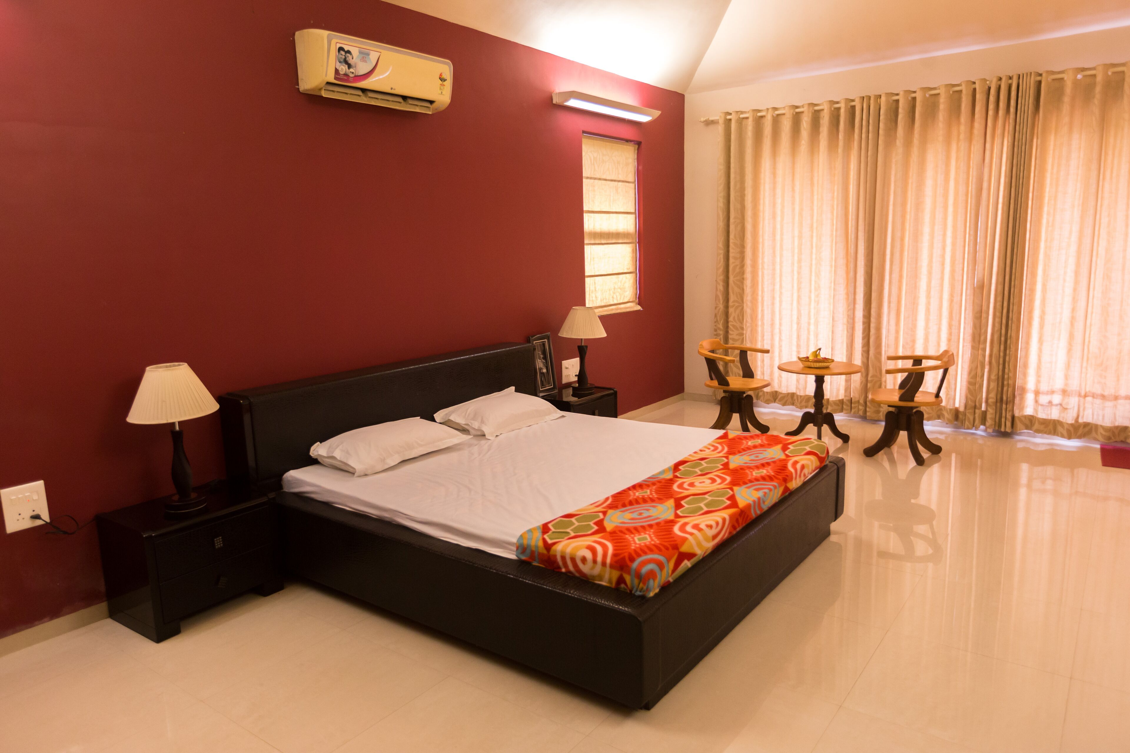 A bedroom with a large bed, bedside tables, a lamp, a small table with chairs, and a window with curtains.