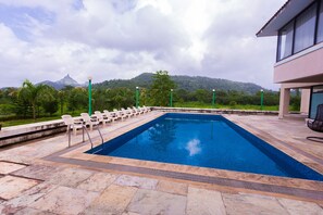 A rectangular swimming pool with a stone deck, surrounded by white lounge chairs and a view of a mountain range.