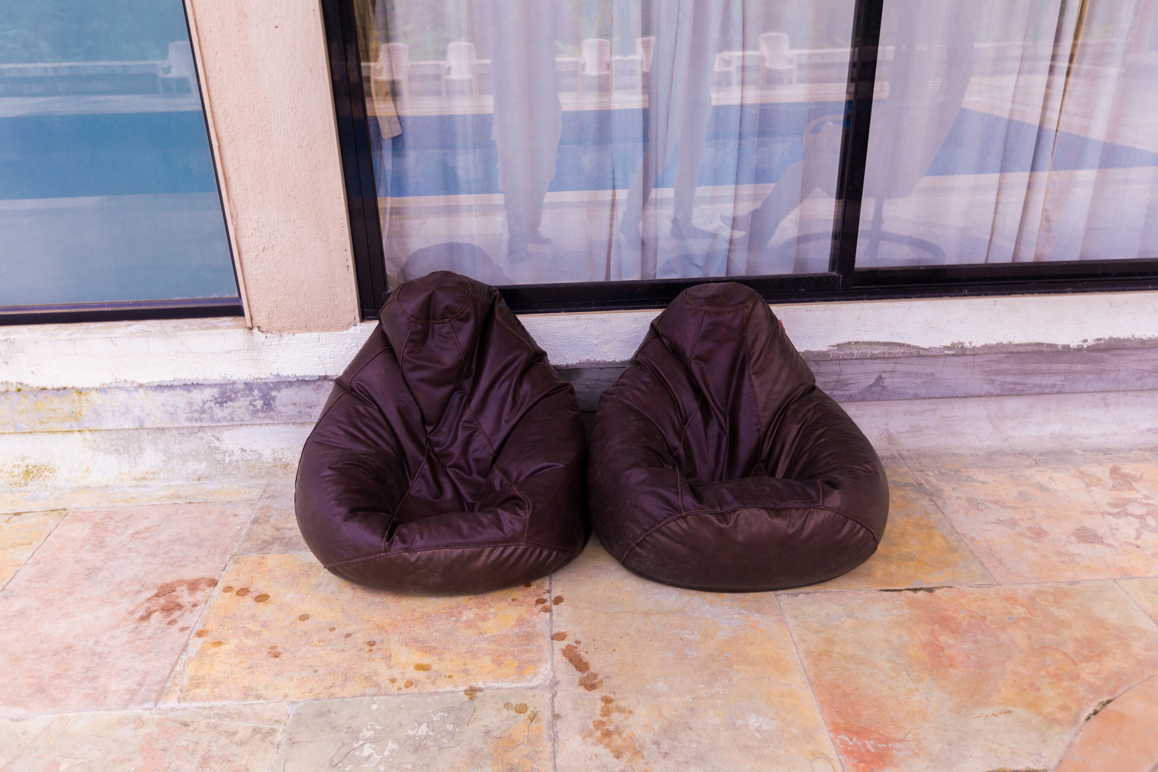 Dois sacos de feijão marrons sobre um chão de azulejos, em frente a um edifício com janelas amplas.