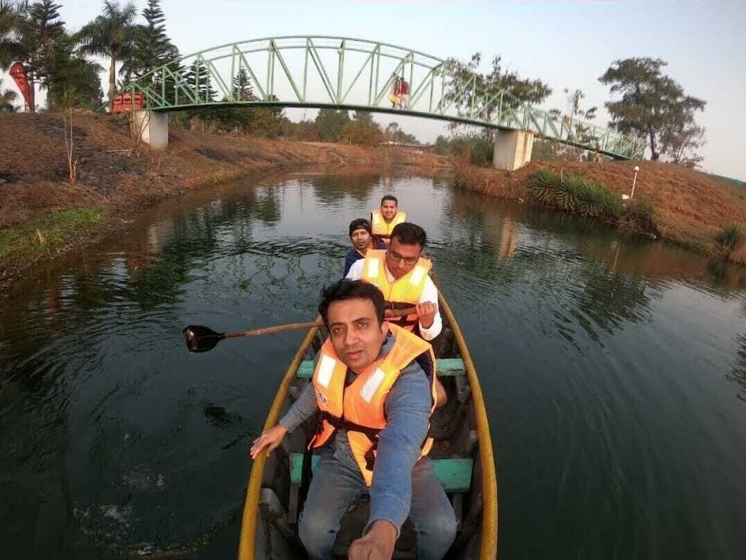 A group of people in a yellow boat on a calm river, wearing life jackets, with a bridge in the background.