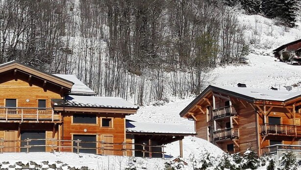 Eine Holzdiele mit einem Balkon, umgeben von schneebedeckten Bäumen und einem See.