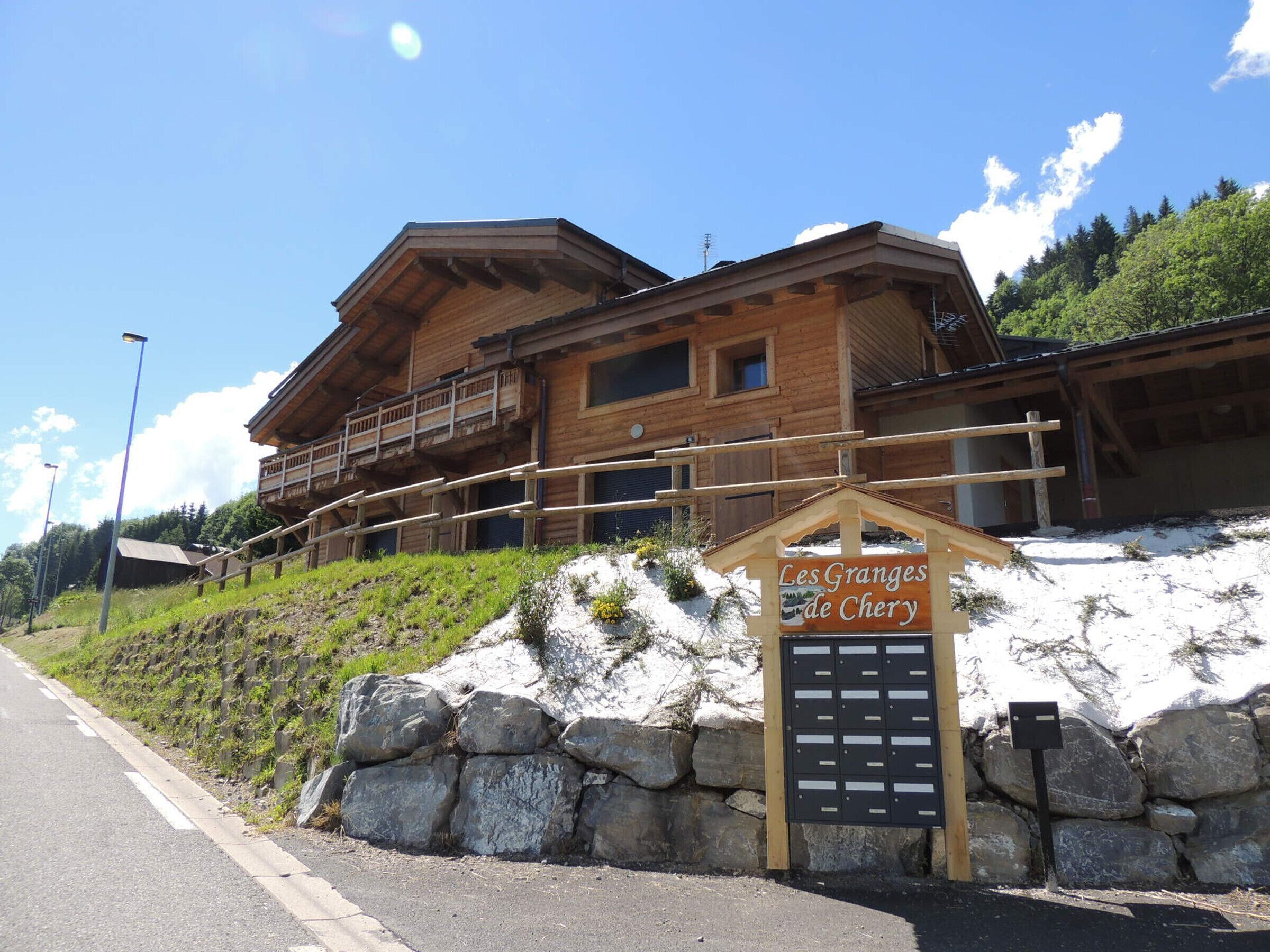 A wooden chalet with a balcony, a stone wall, and a sign reading "Les Granges de Cherry".