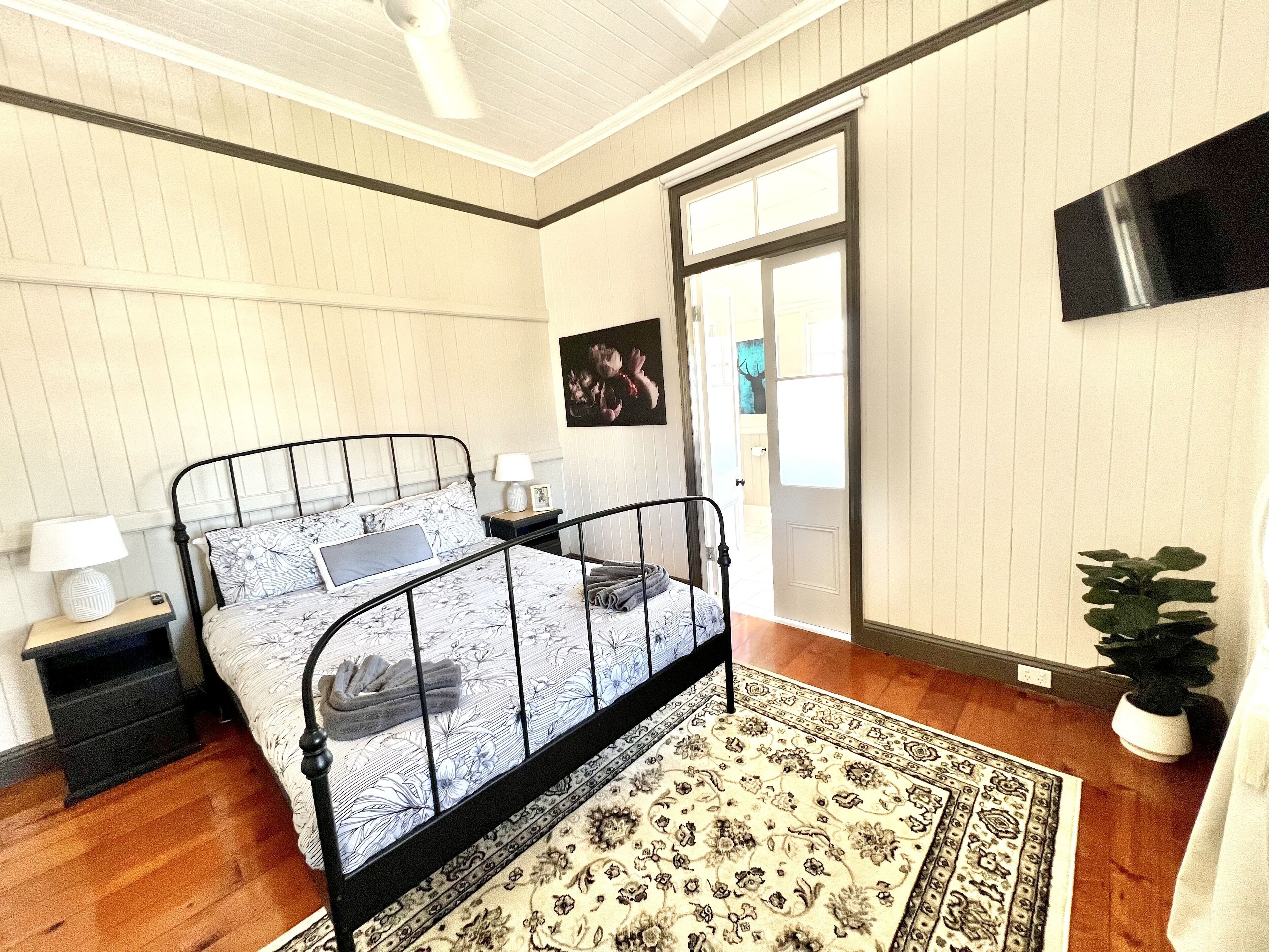 A bedroom with a bed, nightstands, a wall-mounted TV, and a door leading to another room.