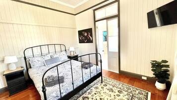 A bedroom with a bed, nightstands, a wall-mounted TV, and a door leading to another room.