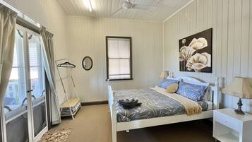 A bedroom with a bed, a nightstand, a hanging lamp, a window with curtains, a ceiling fan, and a painting on the wall.