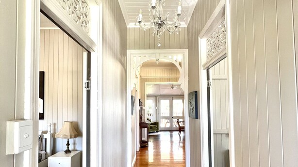 A hallway with wooden flooring, white walls, and a chandelier. There are doors leading to different rooms. - Childers charmer - with aircon, WIFI and modern luxuries (Childers)