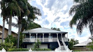 A two-story house with a balcony, surrounded by a white picket fence and palm trees. - Childers charmer - with aircon, WIFI and modern luxuries (Childers)