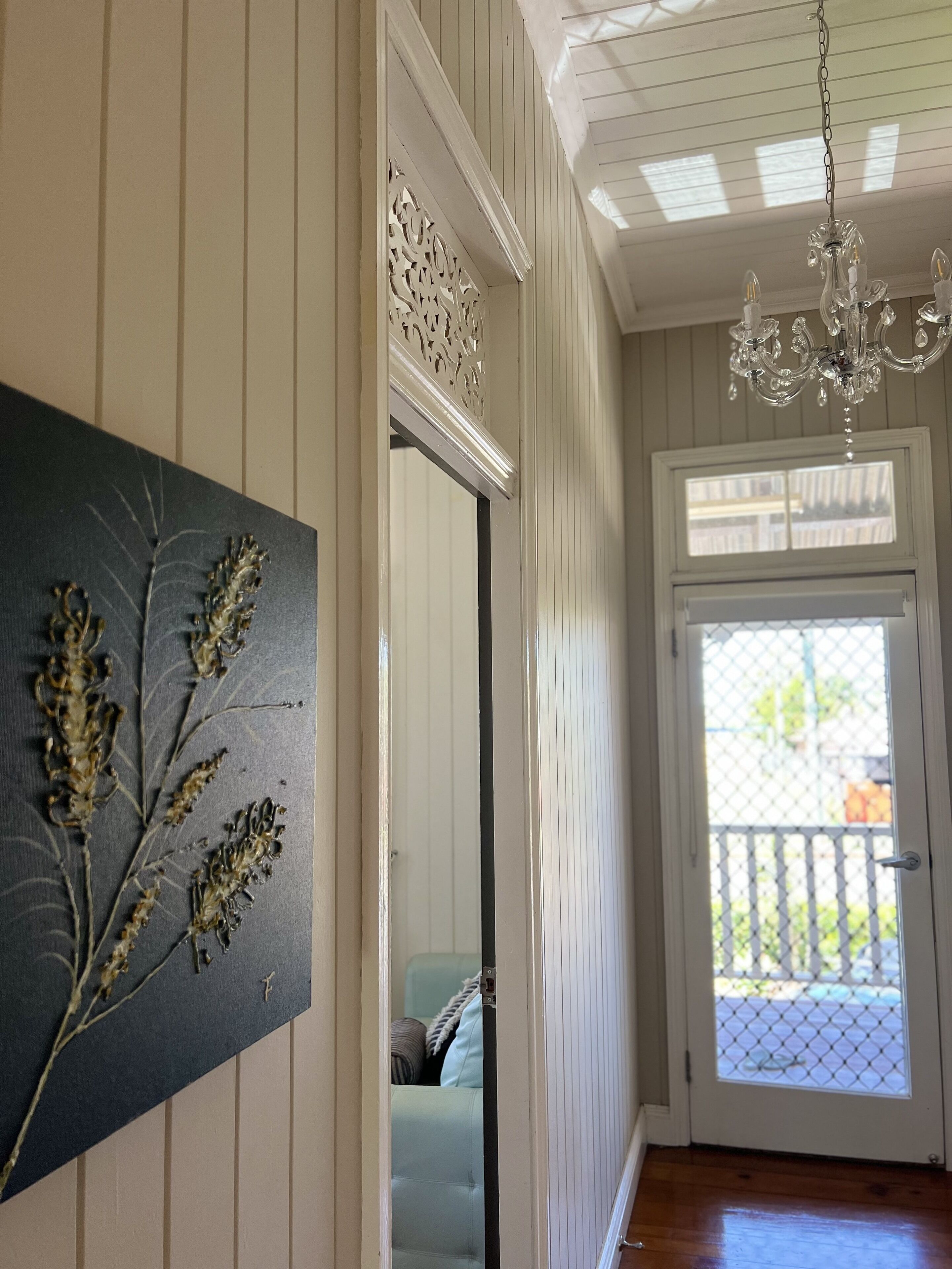 A hallway with a chandelier, a door with a mesh screen, and a wall-mounted artwork.