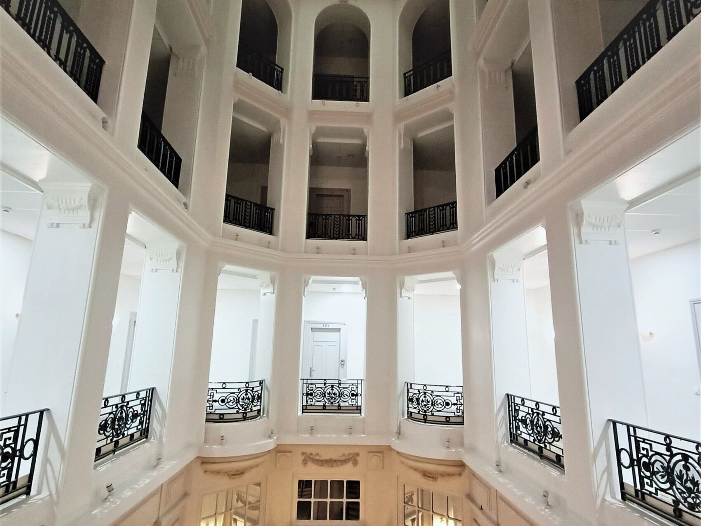 A multi-level atrium with white walls and black railings, featuring a central open space and multiple balconies.