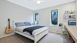 Ein Schlafzimmer mit einem Bett, einer Gitarre, zwei Fenstern und einem Schreibtisch mit Regalen.