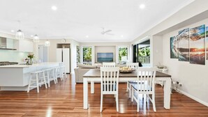 Una cocina amplia con una isla central, un comedor con sillas blancas y un ventanal con vistas al exterior.
