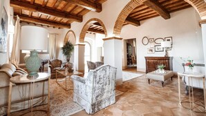 A spacious living area with a high wooden ceiling, arched brick columns, a beige sofa, a marble armchair, and a coffee table.