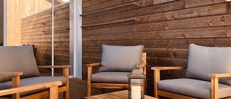 Une terrasse en bois avec deux chaises en bois et une table, une lanterne et une porte-fenêtre coulissante.