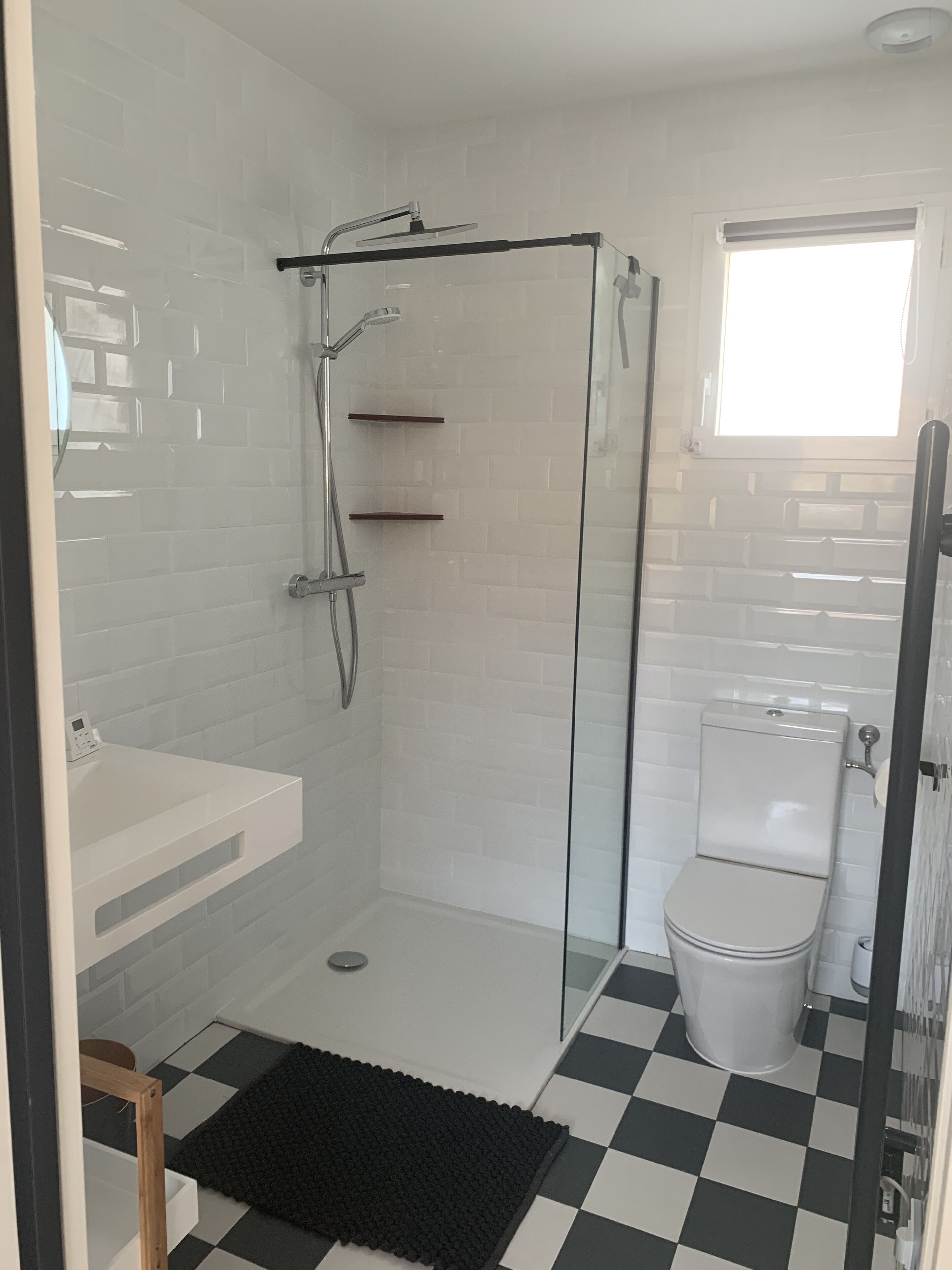 Een badkamer met een douchecabine van glas, een wit toilet en een zwart-wit betegelde vloer.