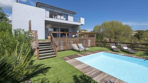 Een modern huis met twee verdiepingen, een zwembad, houten terras en een zitgedeelte buiten.
