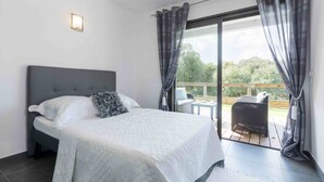 Een slaapkamer met een bed, nachtkastje, raam met gordijnen en uitzicht op het landschap.