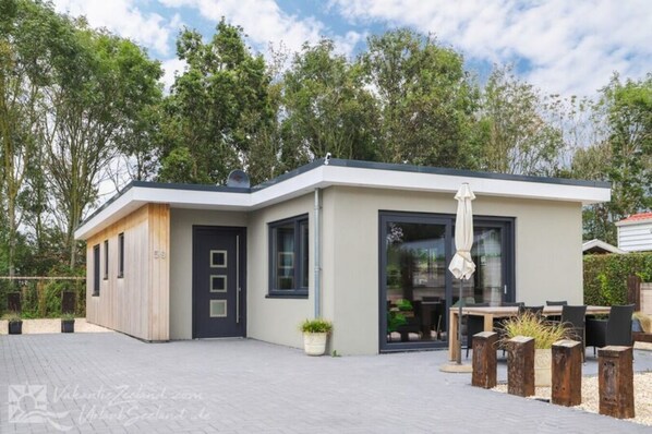 Une maison moderne de plain-pied, dotée d’un toit plat, d’une porte d’entrée sombre et d’une grande porte vitrée donnant sur un patio aménagé avec du mobilier d’extérieur.