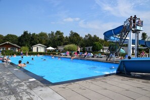 Swimmers enjoy the pool, water slide, and beach chairs in this outdoor pool area.