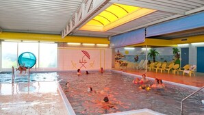 Een binnenzwembad met een strandthema muurschildering, een glijbaan en dakraamverlichting.