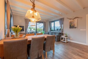 Una sala de estar moderna con una mesa de comedor de madera, asientos cómodos, un ventanal con cortinas y una lámpara colgante.