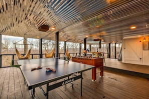 A spacious room with a ping pong table, foosball table, and large windows offering views of the outdoors.