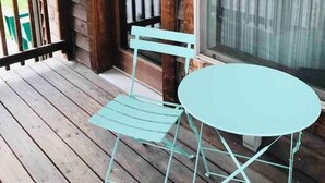 Une terrasse en bois avec une table et une chaise en métal turquoise, une balustrade en bois et une grande fenêtre avec des rideaux.