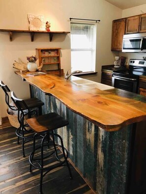 Una cucina con isola in legno, sgabelli da bar, forno integrato e una finestra con persiane.