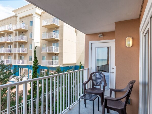 A balcony with two chairs and a table, overlooking a multi-story building with balconies.