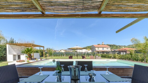 A poolside dining area with outdoor seating and a view of a swimming pool. - Comfortable villa with private swimming pool (Marina di Ascea)