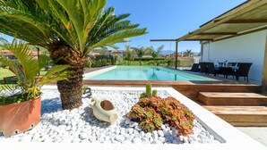 A swimming pool with a white pebble border, surrounded by a palm tree, a cactus, and a potted plant. - Comfortable villa with private swimming pool (Marina di Ascea)