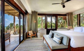 Relax in a spacious room with a large bed, sofa, and chair, offering a view of palm trees and the ocean.