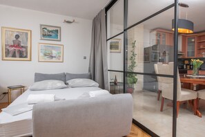 Ett modernt hotellrum med en säng, en stol, ett matbord och ett köksutrymme som syns genom en glasvägg.