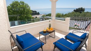 A balcony with two blue cushioned chairs, a small table with a fruit basket, and a view of the sea and greenery. - ☆ Luxury apartment ☆ Heated pool ☆ Private parking (split)