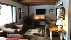 A cozy living room with a stone fireplace, wooden furniture, and a flat-screen TV mounted on the wall.