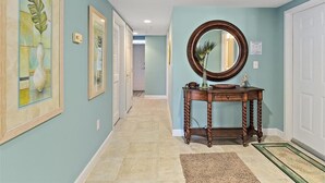 Un pasillo con paredes azul claro, una consola de madera con un espejo y obras de arte enmarcadas.