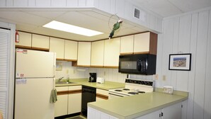 A compact kitchen with a refrigerator, microwave, stove, and a small dining area with stools. - One-bedroom and one and a half bath condo on ocean block! (Ocean City)