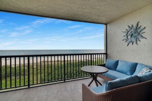 Un balcón con vista a la playa, un sofá de mimbre y una mesita.