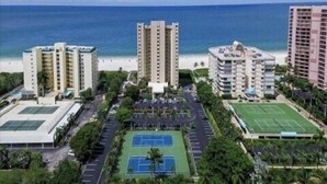 Un hotel moderno de gran altura con varias plantas, una cancha de tenis y vista al mar.