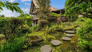 A traditional Japanese-style building with a sloped roof, surrounded by lush greenery and a small pond.