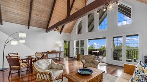 A spacious living room with high ceilings, large windows, and a dining area with wicker furniture.