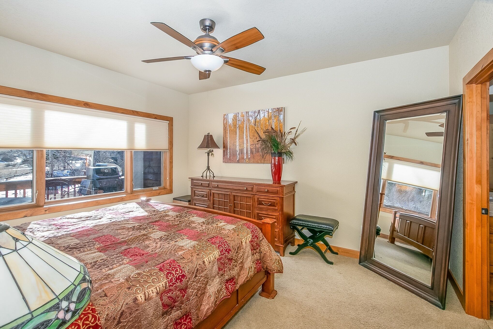 A bedroom with a bed, a dresser, a mirror, a window, and a ceiling fan.