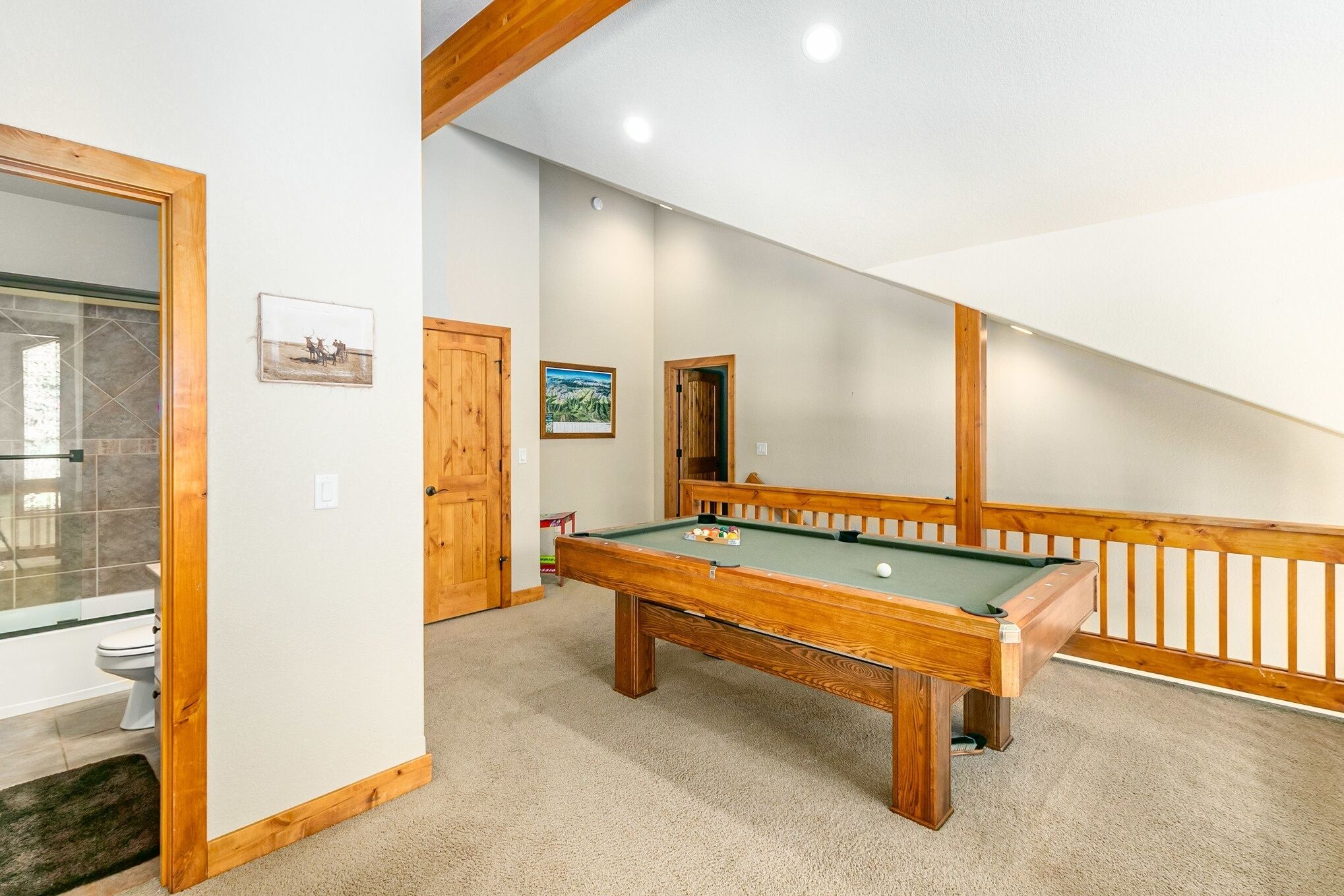 A pool table in a room with a wooden ceiling and a glass door leading to a bathroom.