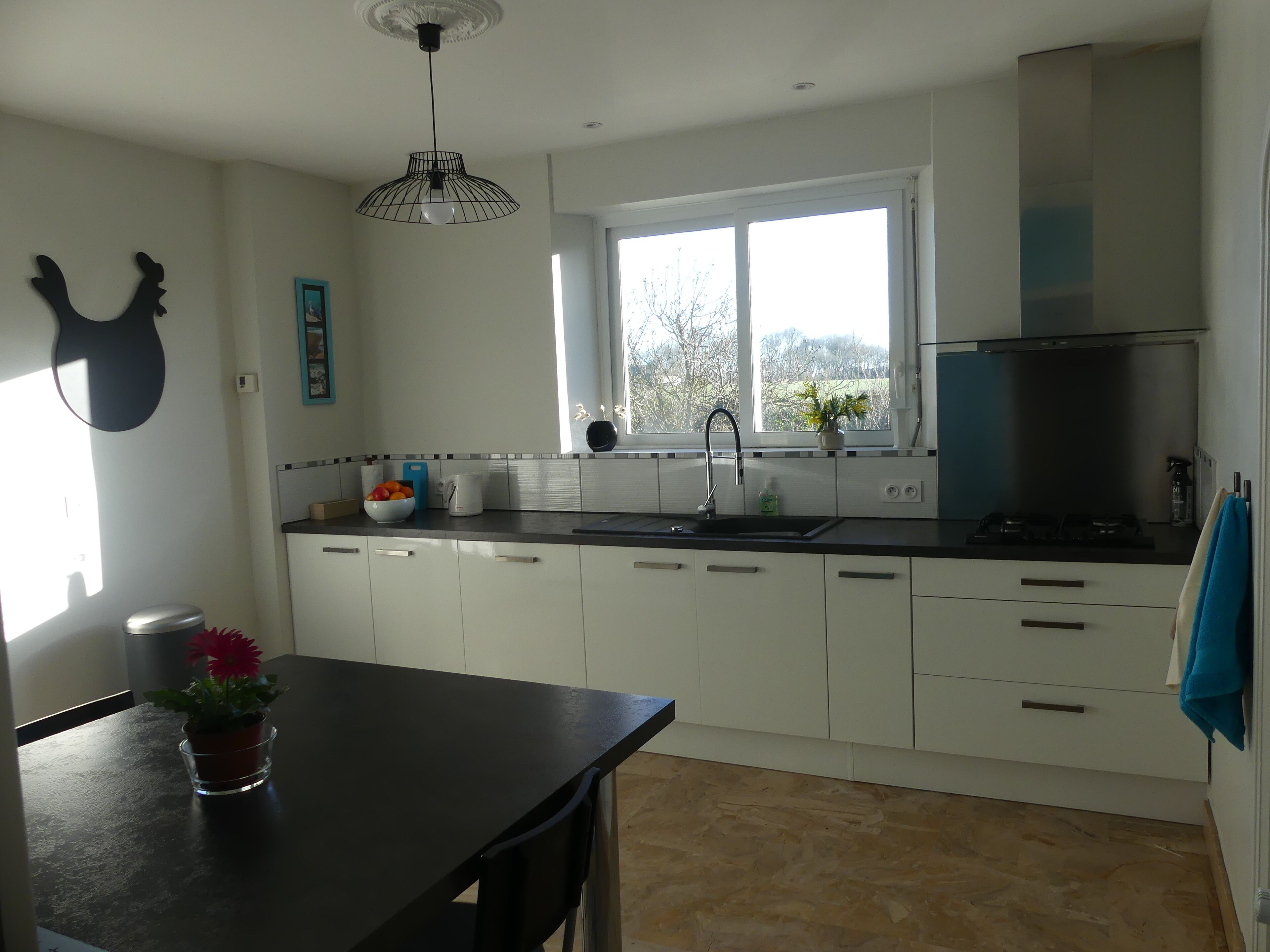 Cocina moderna con armarios blancos, encimera negra, ventana con vistas y lámpara colgante.