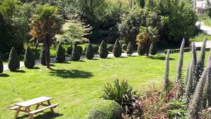 A well-maintained garden with neatly trimmed hedges, a picnic table, and a variety of trees and shrubs.