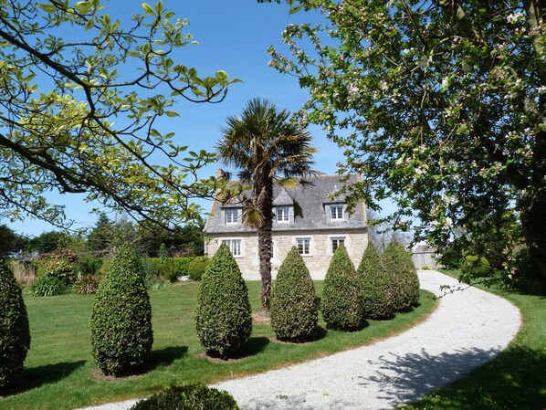 A stone house with a gravel driveway, surrounded by well-manicured hedges and trees. - Charming property 3 km from the beach, with a covered swimming pool (Cléder)