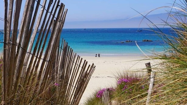 A sandy beach path leading to a beach with clear blue water and distant mountains.
