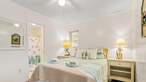 Une chambre à coucher comprenant un lit, deux tables de chevet, une fenêtre avec des stores et un ventilateur de plafond.